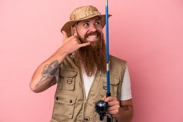 Young caucasian ginger fisherman with long beard holding a rod isolated on pink background showing a mobile phone call gesture with fingers.