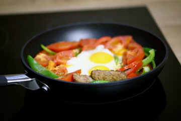 Frying pan with healthy food on a black hob.