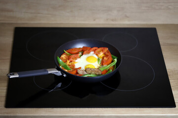 Frying pan with healthy food on a black hob.