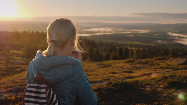 A woman with a backpack behind her drink ay and admires the beautiful nature of Scandinavia