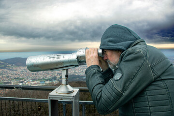 A man with a hood watching the surroundings from the top of the mountain, on a cloudy day.