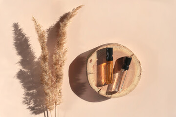 Two glass perfume samples on a wooden tray lying on a beige background with pampas grass. Luxury and natural cosmetics presentation. Testers on a woodcut in the sunlight. Top view