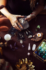 A woman shows the deck of tarot cards ready to begin reading on her witch altar with several semi-precious stones on the table
