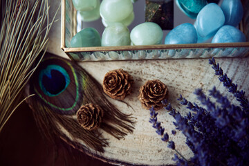 Detail of three pineapples on a wooden trunk next to a glass jewelry box with semiprecious stones in green and turquoise tones. Decorated with some lavender branches and a peacock feather - Powered by Adobe