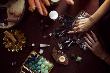 Top view of a tarot card spread. A woman points to one of the cards on her witch altar with several...