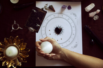 Top view of a woman with long nails holding a selenite crystal ball over her witch altar