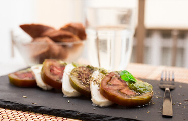 caprese salad with mozzarella, black tomatoes and pesto on black stone plate