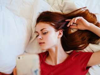 Fototapeta premium woman lies in the sleeping room on the bed with the phone communicating