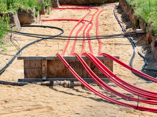 Cables with red electrical insulation lay underground near the distribution building. - 463392317
