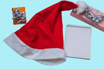 Beautiful view of red Santa hat, pen, gift box and notebook on blue background. Christmas concept. Sweden. 
