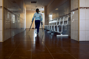 Child walks along hospital corridor on crutches to see doctor. Girl has one leg broken in cast.