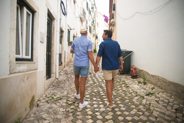 Obraz na płótnie Canvas Back view of happy gay couple. Two men in casual clothes walking in street, looking at each other, having vacation. Love, affection, relationship concept