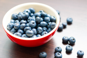 Blueberries in a red bowl on wooden table.