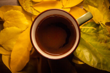 Warm cup of coffee on top of yellow leaves. Perfect moody and bright photo. Moon shape on top of the dark coffee. Autumn vibe. Green coffee mug.