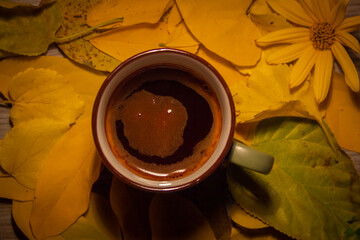 Warm cup of coffee on top of yellow leaves. Perfect moody and bright photo. Moon shape on top of the dark coffee. Autumn vibe. Green coffee mug.