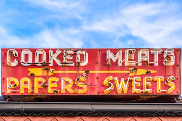 Fototapeta premium A vintage Australian corner shop neon sign with the words 'Cooked Meats' and 'Papers' 'Sweets'
