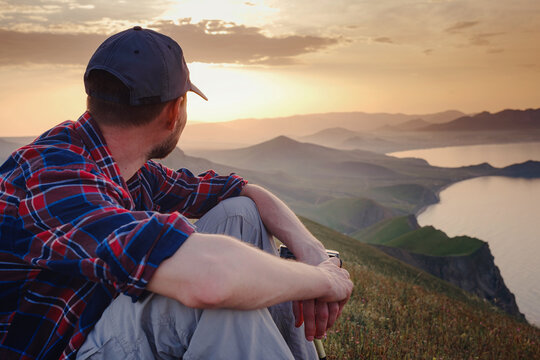 Confident man sitting and enjoying view in hilly landscape far from people. Tourist photographer is relaxing in nature during sunset. Adventure, Travel and Hike concept.