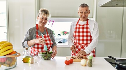Senior caucasian couple smiling happy cooking at the kitchen.