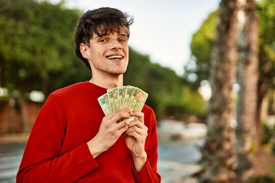 Young hispanic man smiling happy holding argentinian pesos banknotes at the city