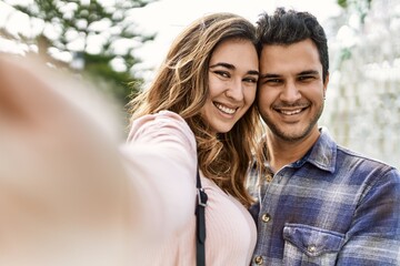 Fototapeta premium Young hispanic couple hugging in love at the city. Girlfriend and boyfriend together in love taking selfie picture