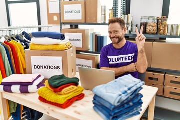 Middle age man wearing volunteer t shirt working with laptop smiling with happy face winking at the...