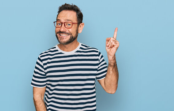 Middle age man wearing casual clothes and glasses with a big smile on face, pointing with hand and finger to the side looking at the camera.
