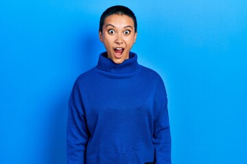 Beautiful hispanic woman with short hair wearing turtleneck sweater afraid and shocked with surprise expression, fear and excited face.