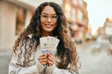 Foto op Canvas Young latin woman smiling happy holding colombia pesos banknotes at the city. © Krakenimages.com