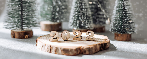 Beautiful New Year greeting card. Decorative numbers 2022 on wooden stand and green fir trees on...