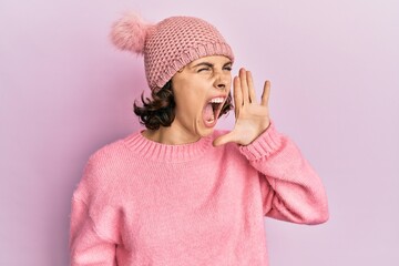 Young brunette woman wearing cute wool cap shouting and screaming loud to side with hand on mouth. communication concept.