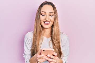 Young blonde girl using smartphone typing message smiling and laughing hard out loud because funny crazy joke.