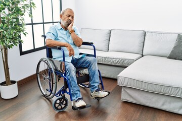 Handsome senior man sitting on wheelchair at the living room thinking looking tired and bored with depression problems with crossed arms.