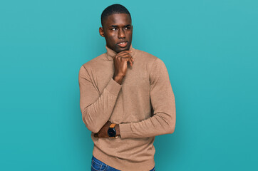 Young african american man wearing casual winter sweater with hand on chin thinking about question, pensive expression. smiling with thoughtful face. doubt concept.