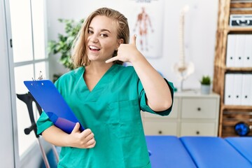 Young caucasian woman working at pain recovery clinic smiling doing phone gesture with hand and fingers like talking on the telephone. communicating concepts.