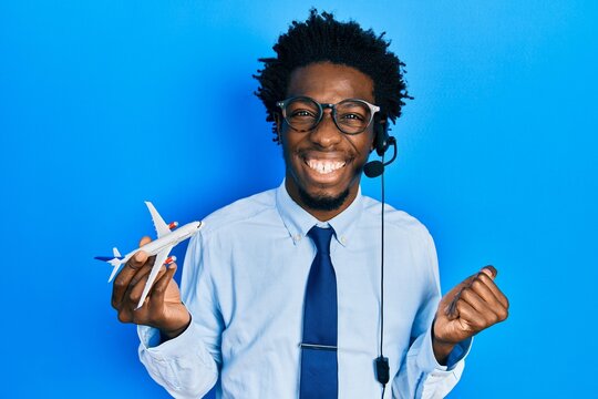 Young african american travel agent man holding plane screaming proud, celebrating victory and success very excited with raised arm