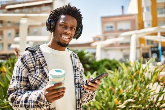 Handsome black man with afro hair wearing headphones listening to music using smartphone