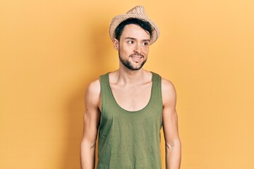 Young hispanic man wearing summer hat looking away to side with smile on face, natural expression. laughing confident.