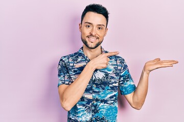 Young hispanic man wearing casual clothes amazed and smiling to the camera while presenting with hand and pointing with finger.