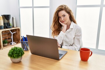 Young caucasian woman working at the office using computer laptop thinking looking tired and bored with depression problems with crossed arms.