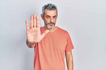 Handsome middle age man with grey hair wearing casual t shirt doing stop sing with palm of the hand. warning expression with negative and serious gesture on the face.