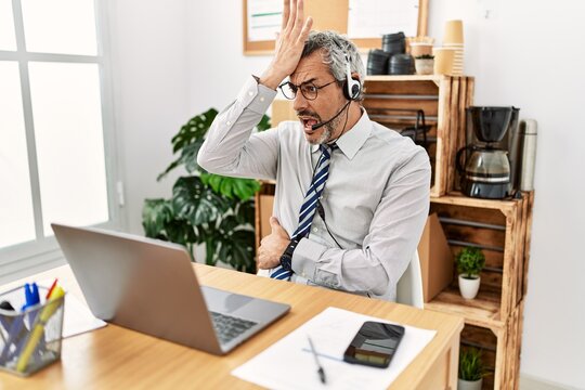 Middle age hispanic business man working at the office wearing operator headset surprised with hand on head for mistake, remember error. forgot, bad memory concept.