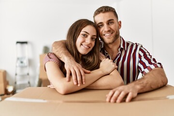Young caucasian couple smiling happy leaning on cardboard box at new home.