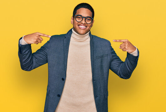 Young handsome hispanic man wearing business jacket and glasses looking confident with smile on face, pointing oneself with fingers proud and happy.