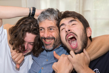 Fototapeta premium Père qui joue, qui chahute avec ses deux grands enfants adolescents. Ils sont fun et drôles, ils s'amusent. 