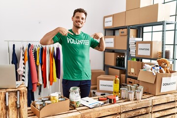 Young hispanic man pointing with fingers to volunteer uniform at charity center