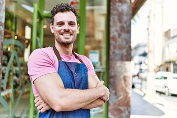 Fototapeta premium Young hispanic waiter wearing apron standing with arms crossed gesture at coffee shop.