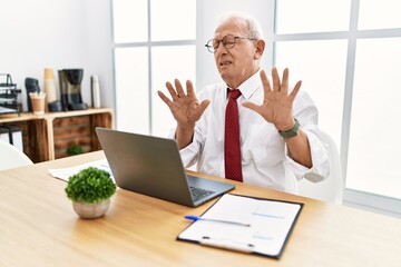 Senior man working at the office using computer laptop moving away hands palms showing refusal and...