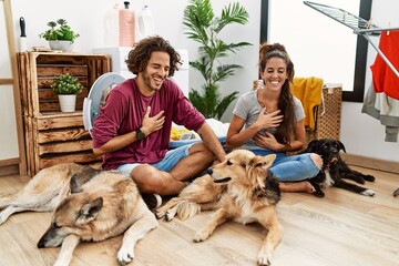 Young hispanic couple doing laundry with dogs smiling and laughing hard out loud because funny crazy joke with hands on body.