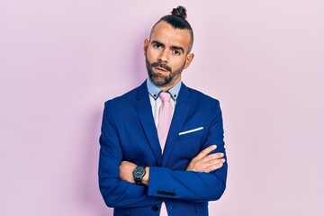 Young hispanic man wearing business suit with arms crossed gesture in shock face, looking skeptical and sarcastic, surprised with open mouth