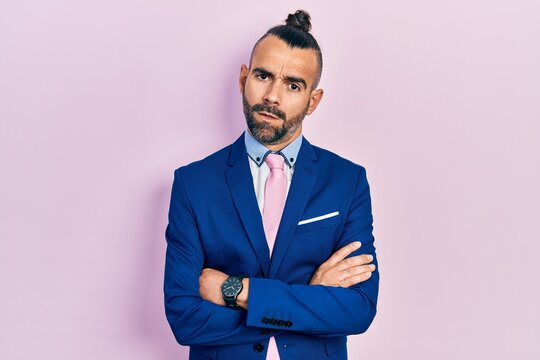 Young hispanic man wearing business suit with arms crossed gesture in shock face, looking skeptical and sarcastic, surprised with open mouth